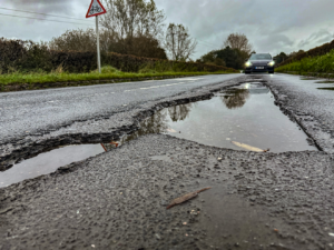 Rain-filled potholes on a rural road in the UK. How to claim if you hit a pothole.